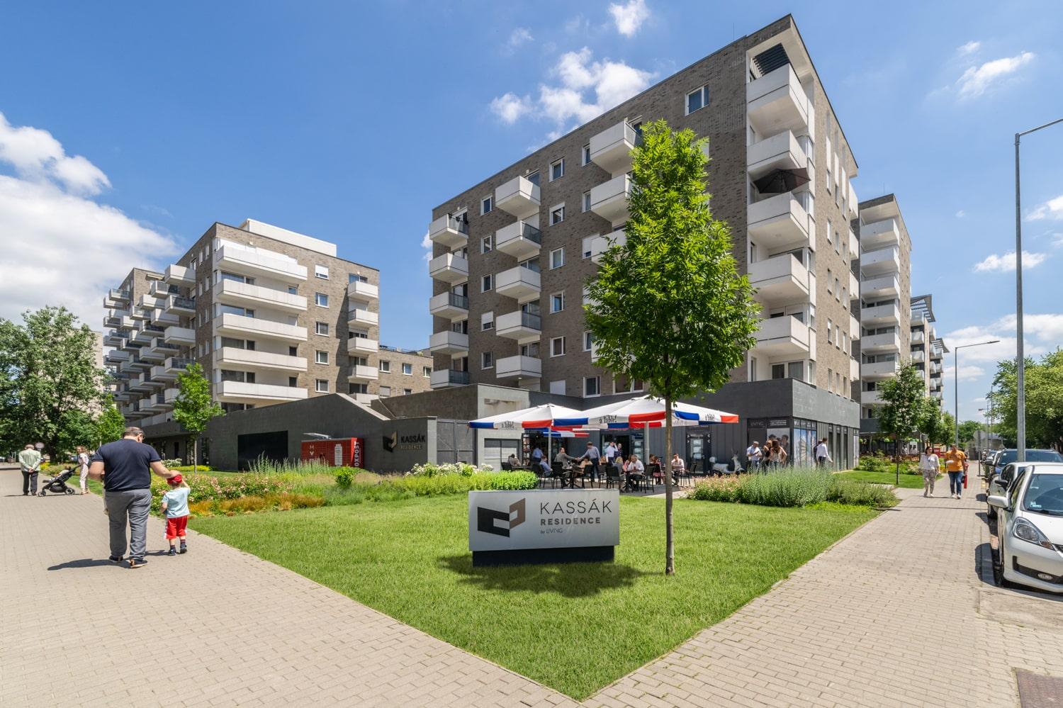 Kassák Residence lakópark és alatta egy üzlethelyiség sétáló emberekkel